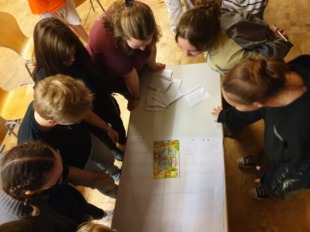 Bild von Oben mit Blick auf eine Gruppe Jugendlicher, die ein Puzzel Rätzel lösen